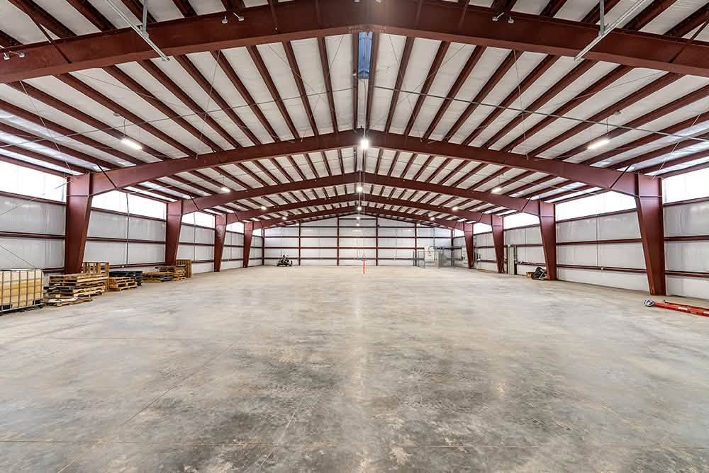 Clear-span commercial steel building interior with red structural framing and concrete slab by B&J Metal Buildings.