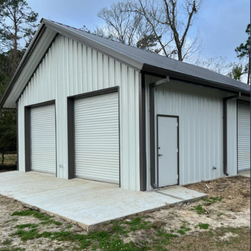 White metal garage with three roll-up doors, a walk door and concrete foundation by B&J Metal Buildings.